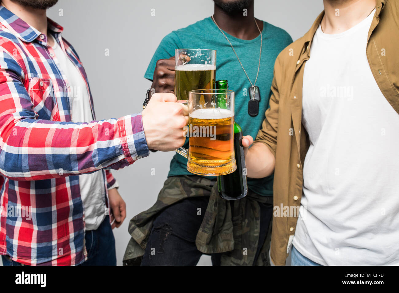 Près de trois jeunes hommes heureux de trinquer avec des verres de bière isolé sur gray Banque D'Images
