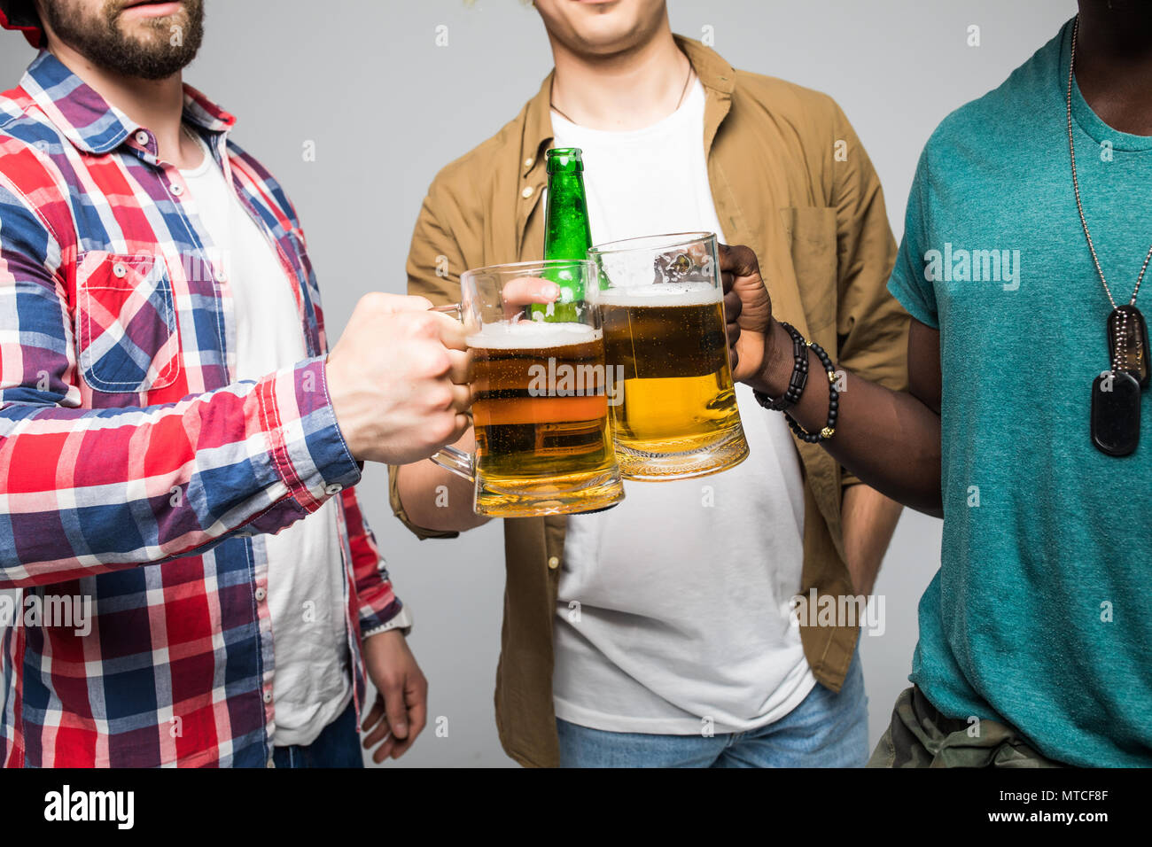 Près de trois jeunes hommes heureux de trinquer avec des verres de bière isolé sur gray Banque D'Images