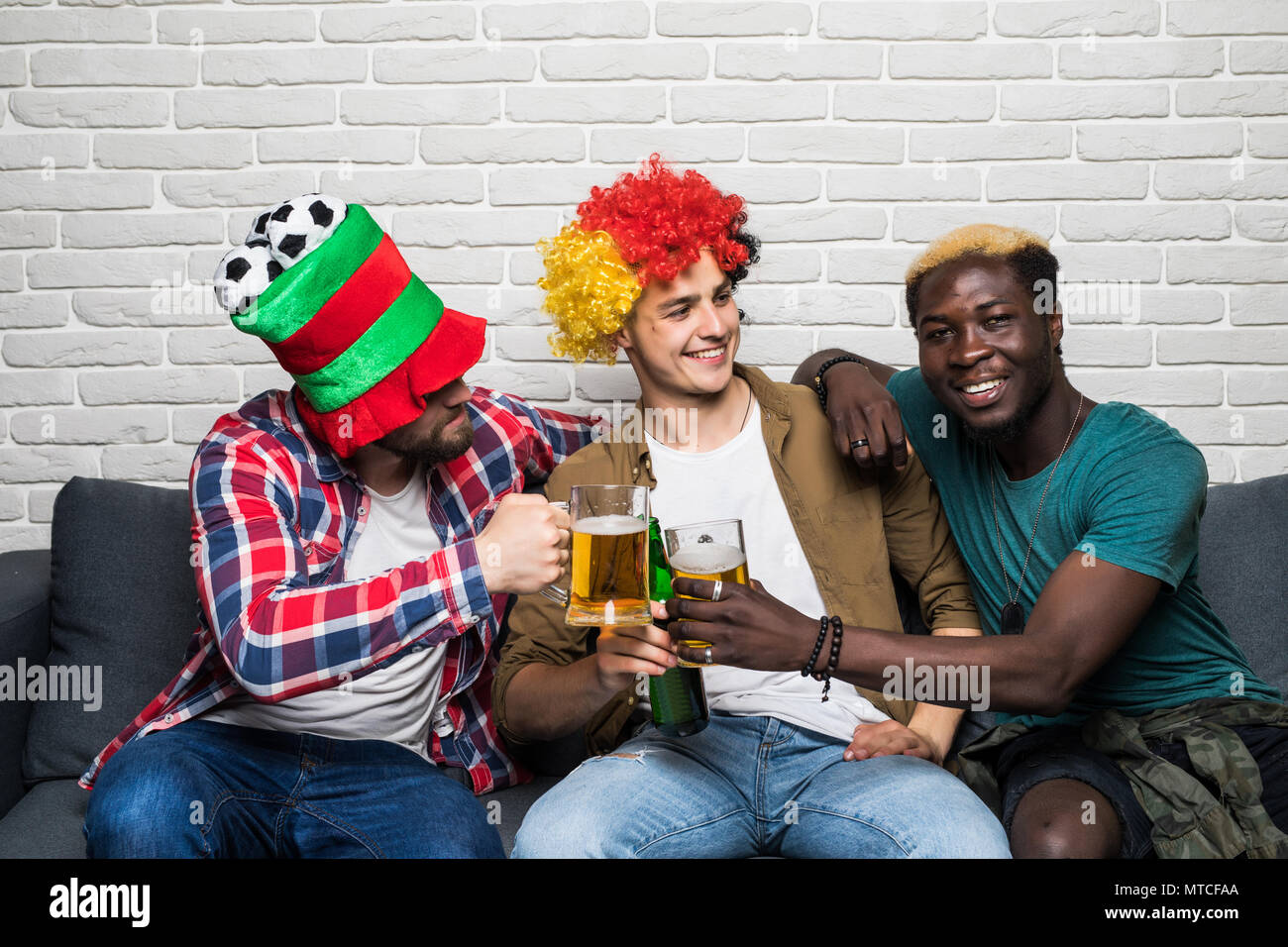 Trois hommes heureux assis sur table et regarder les sports à la télévision. Banque D'Images