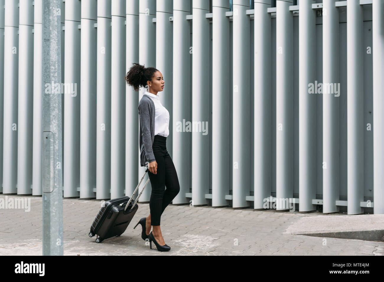 Businesswoman with rolling suitcase walking on street, side view Banque D'Images