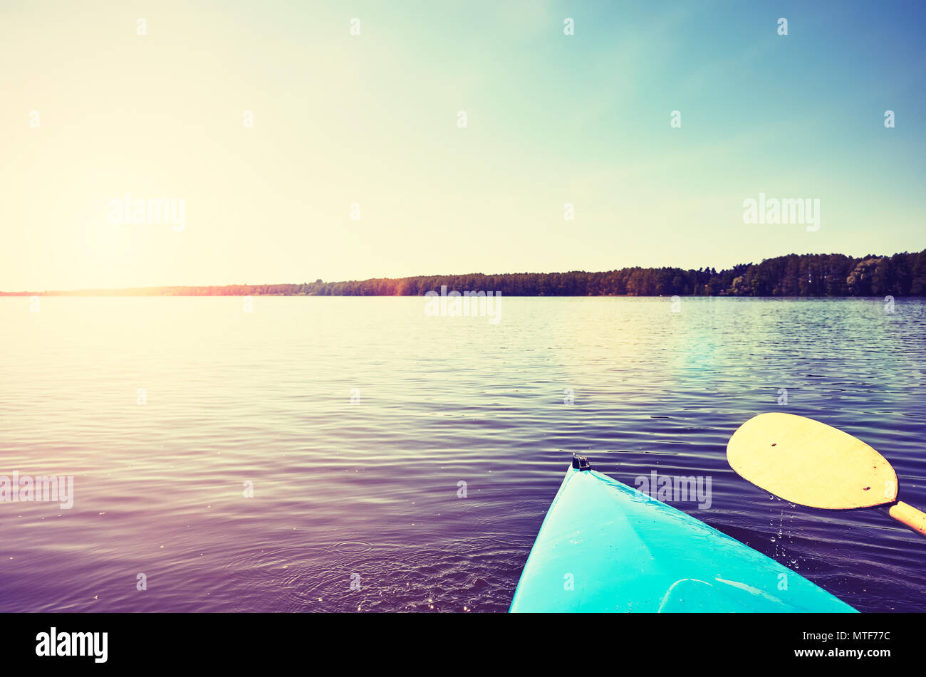 Proue d'un kayak avec pagaie sur un lac au coucher du soleil, toujours dans des tons de couleur photo, selective focus. Banque D'Images Proue d'un kayak avec pagaie sur un lac au coucher du soleil, toujours dans des tons de couleur photo, selective focus. Banque D'Images