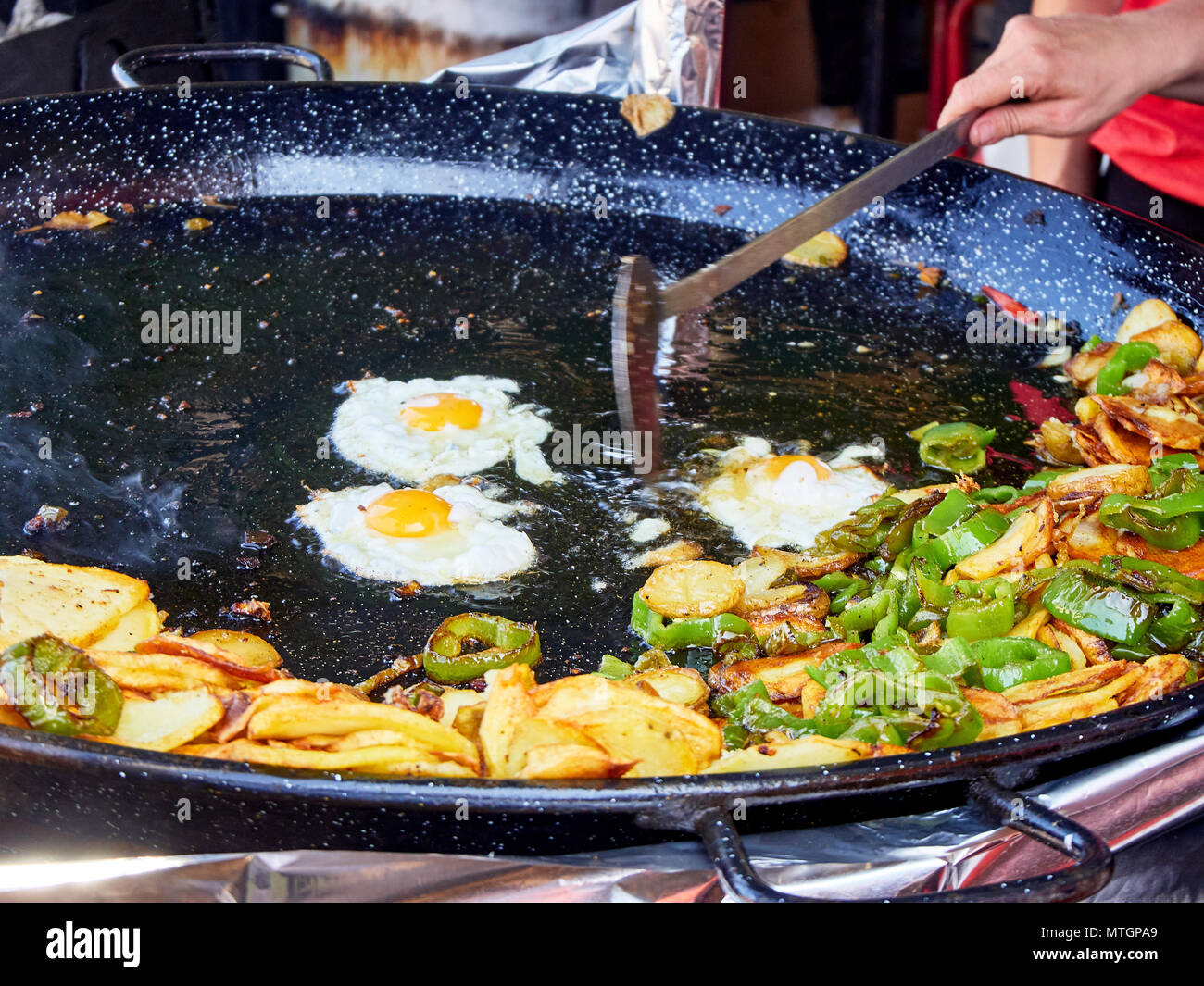 Les oeufs en cours d'espagnol. Oeufs au plat avec les pommes de terre et les poivrons dans la poêle. L'alimentation de rue en espagnol. Banque D'Images