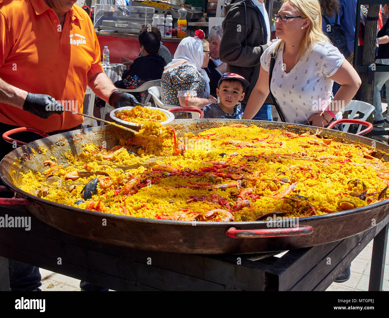 Madrid, Espagne - 15 mai 2018. Un cuisinier espagnol Vente de paella dans un stand à une foire gastronomique sous l'œil attentif d'un garçon asiatique. Banque D'Images