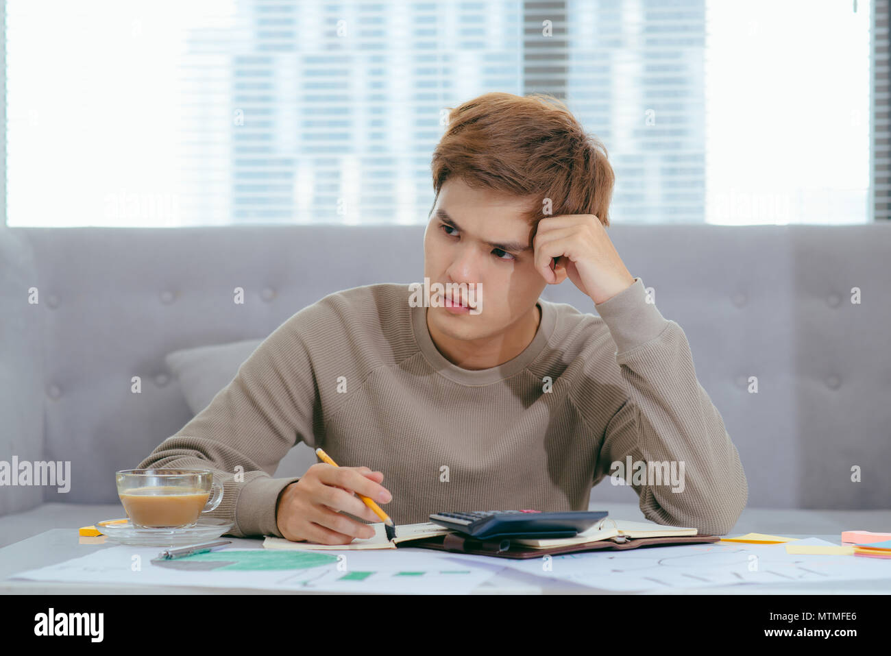 Young attractive Young Asian man sitting on sofa at home avec la calculatrice des coûts comptables, frais, taxes et hypothèque pour payer les factures à la worrie Banque D'Images