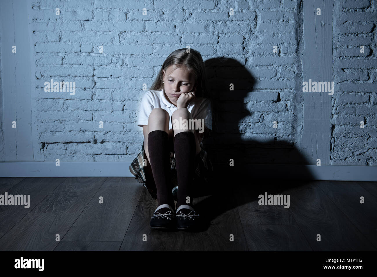 Désespérément triste jeune fille souffrant de bulling et abattage harcèlement seul, malheureux et sans espoir désespéré assis contre le mur, Lumière sombre. Sc Banque D'Images