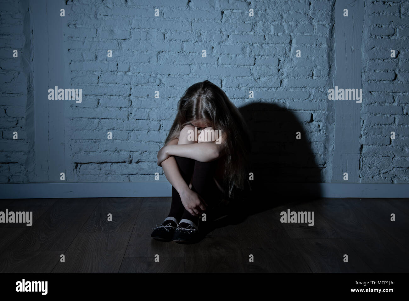 Désespérément triste jeune fille souffrant de bulling et abattage harcèlement seul, malheureux et sans espoir désespéré assis contre le mur, Lumière sombre. Sc Banque D'Images