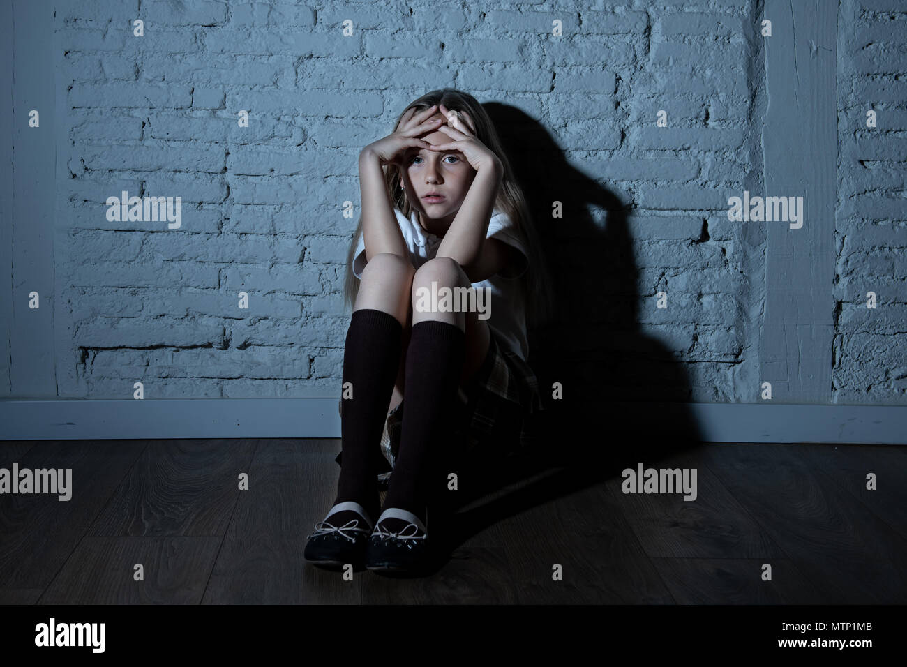 Désespérément triste jeune fille souffrant de bulling et abattage harcèlement seul, malheureux et sans espoir désespéré assis contre le mur, Lumière sombre. Sc Banque D'Images