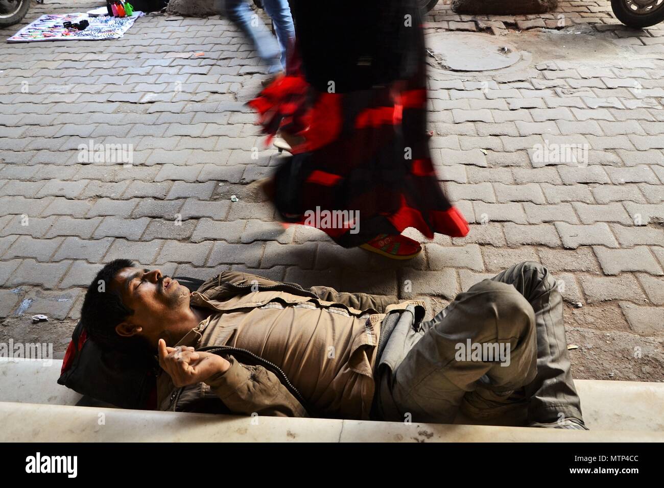 Un homme fatigué de dormir sur le trottoir comme les passants à pied passé dans Chandni Chowk marché dans la vieille ville de Delhi Banque D'Images