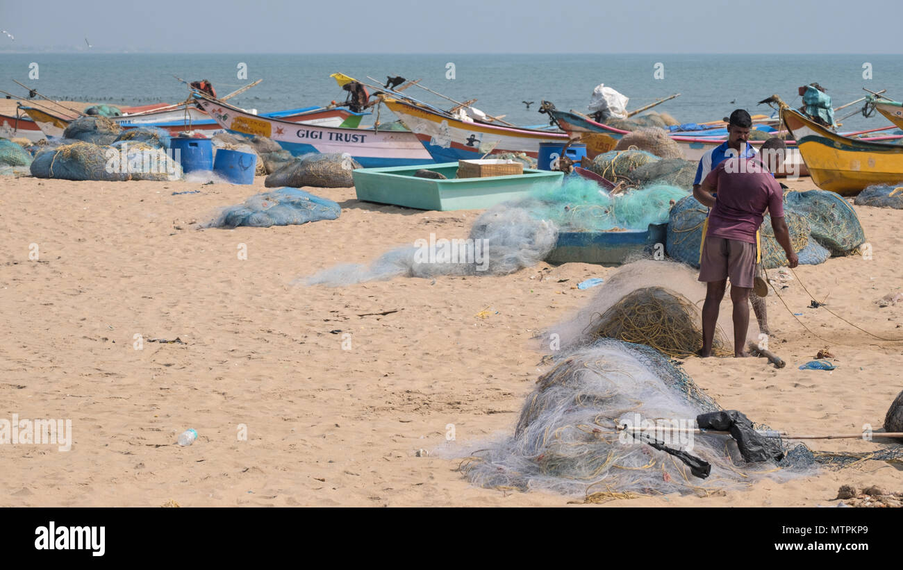 Kovalam, Inde - 20 mars 2018 : les pêcheurs réparant leurs filets aux côtés de bateaux sur la côte de Coromandel. Les principales captures locales sont pomfrets et langoustines Banque D'Images