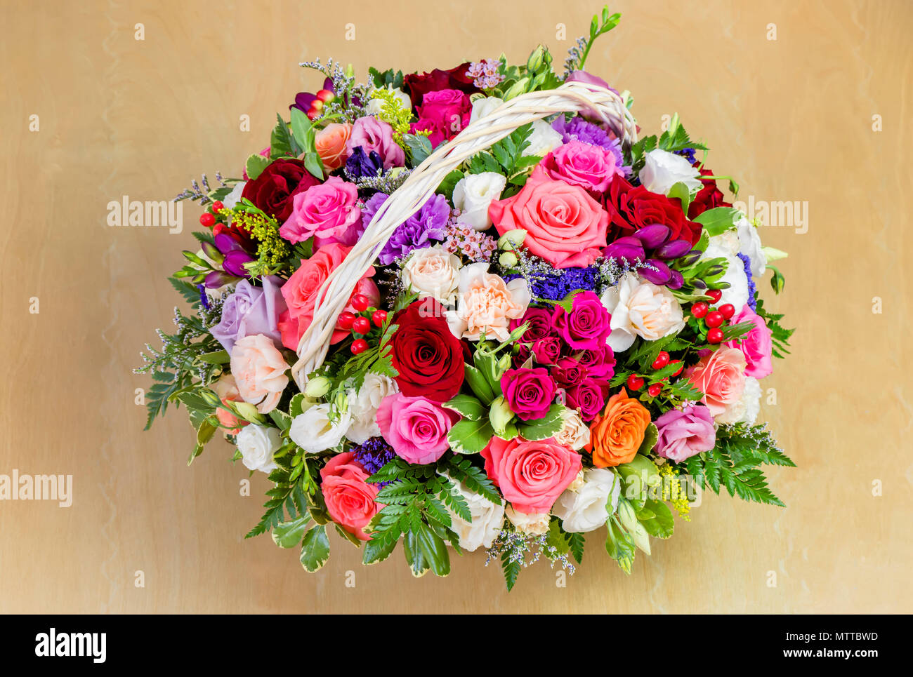 Vue de dessus de roses rouges et jaunes avec des feuilles vertes dans un panier sur une table en bois Banque D'Images