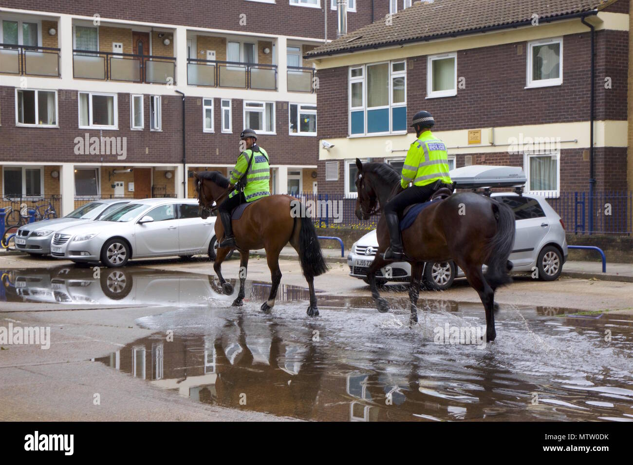 Deux policiers métropolitains qui sont des chevaux de course au trot dans une flaque d'eau sur le chemin de l'équitation dans la région de Bow, Tower Hamlets, London Banque D'Images