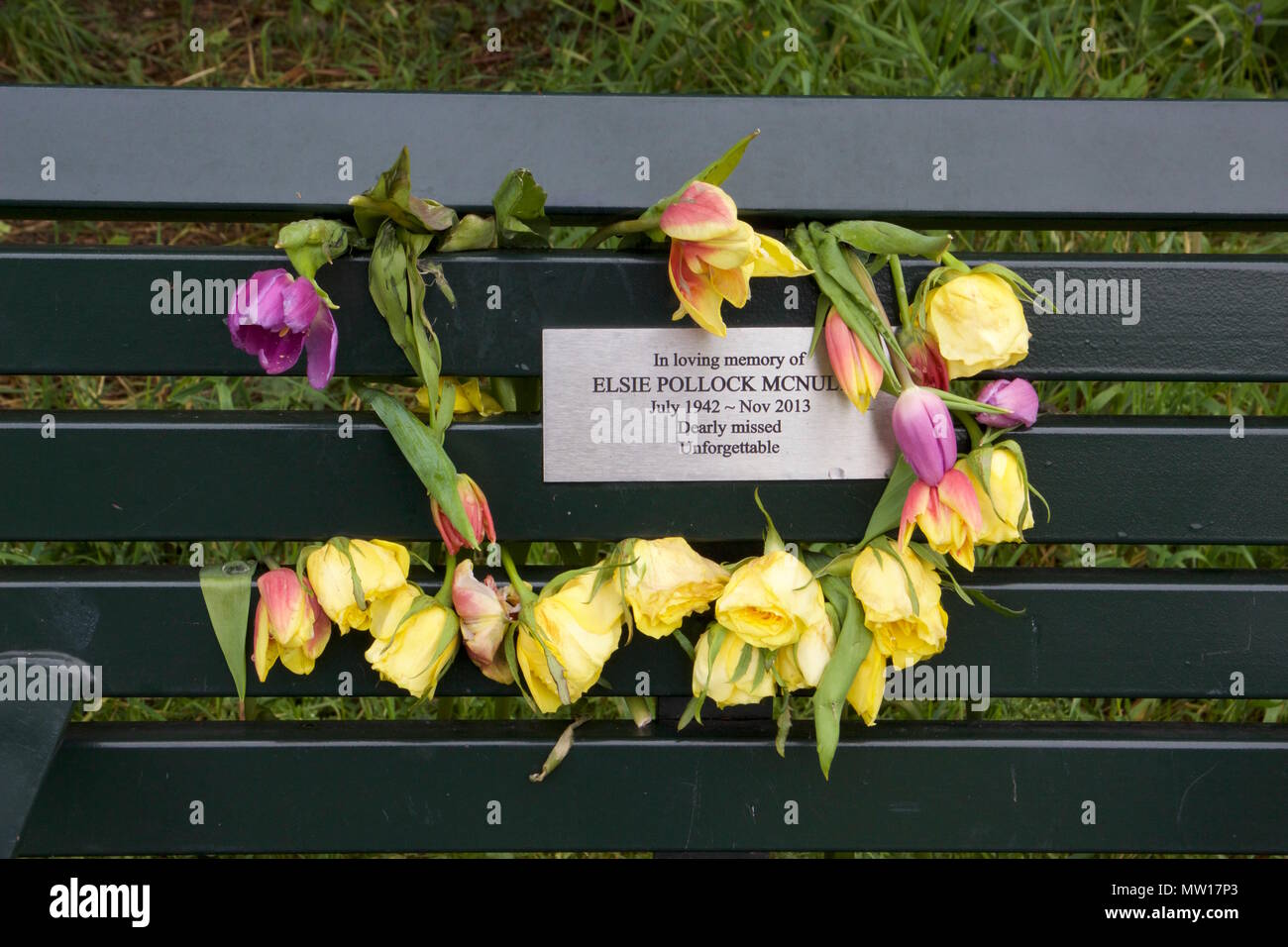 Un mémorial banc avec une plaque métallique entouré de fleurs en train de mourir à l'intérieur de Tower Hamlets Cemetery Park Banque D'Images