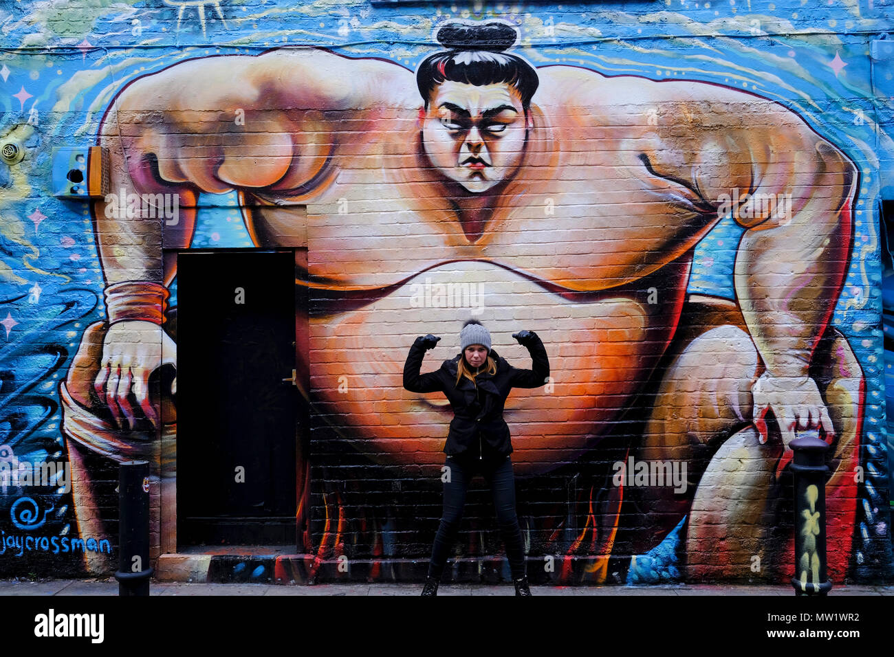Une femme est debout devant l'énorme graffiti japonais du lutteur poids lourd Sumo à Brick Lane, Londres, Royaume-Uni. Banque D'Images Une femme est debout devant l'énorme graffiti japonais du lutteur poids lourd Sumo à Brick Lane, Londres, Royaume-Uni. Banque D'Images
