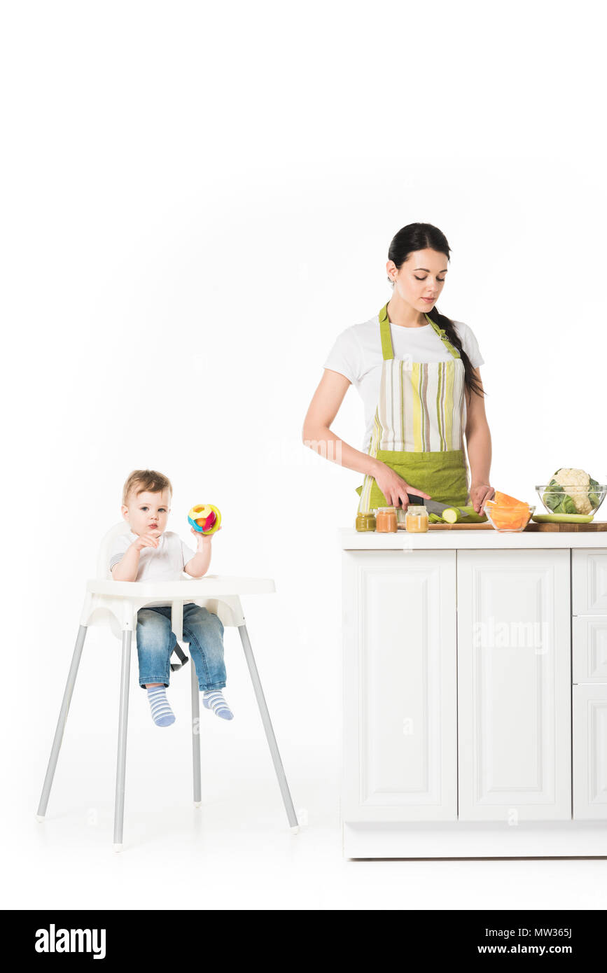 Chaise haute bébé garçon avec toy et mère de courgettes coupe à table isolé sur fond blanc Banque D'Images