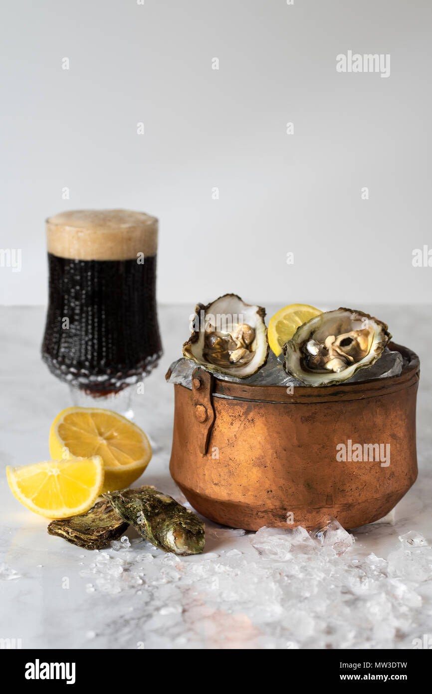 Huîtres crues dans la glace dans un seau en cuivre avec du citron et un verre de bière piquant Banque D'Images