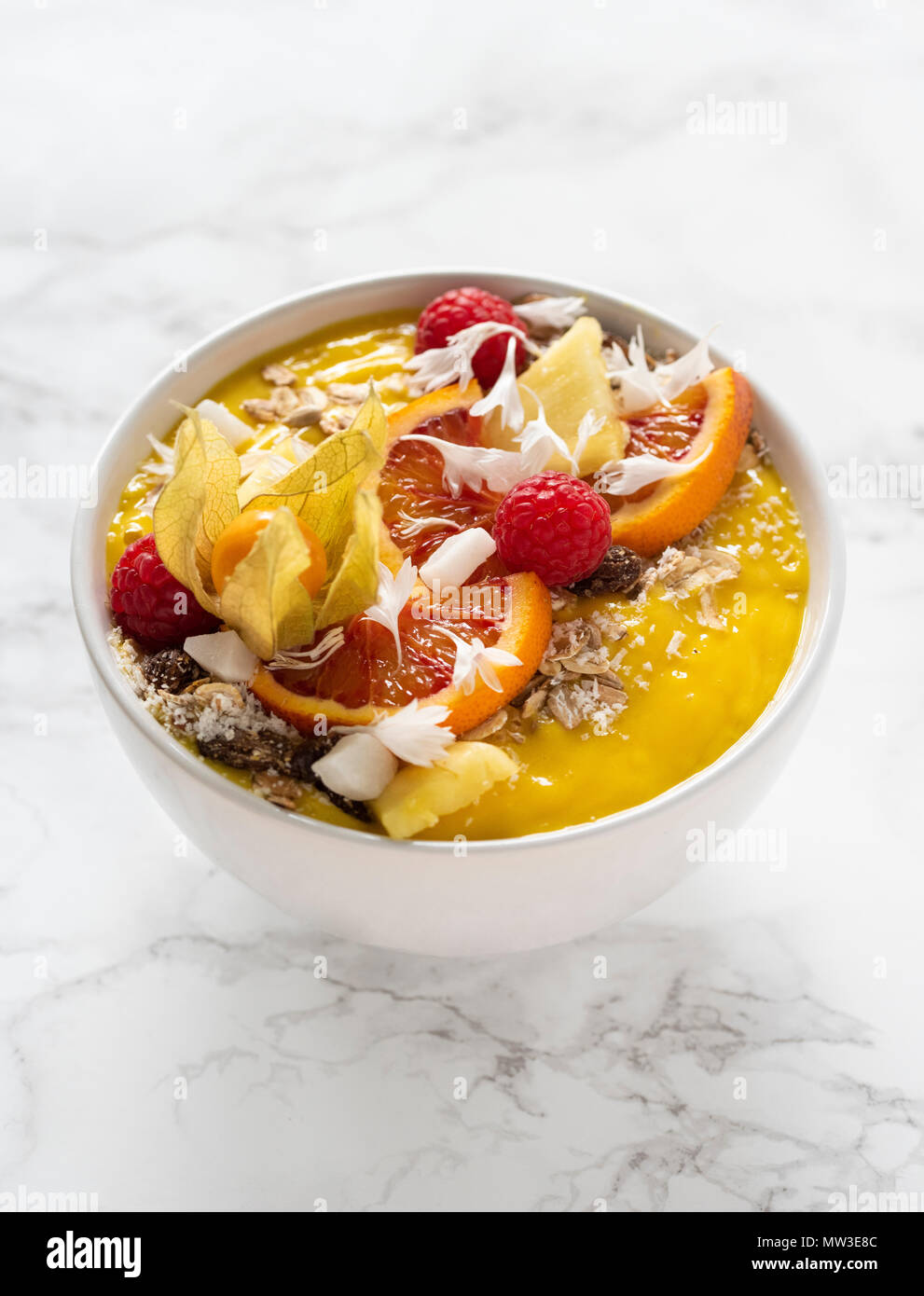 Smoothie mangue jaune à décor d'granola, baies, fruits, flocons de noix de coco sur une base en marbre blanc Banque D'Images