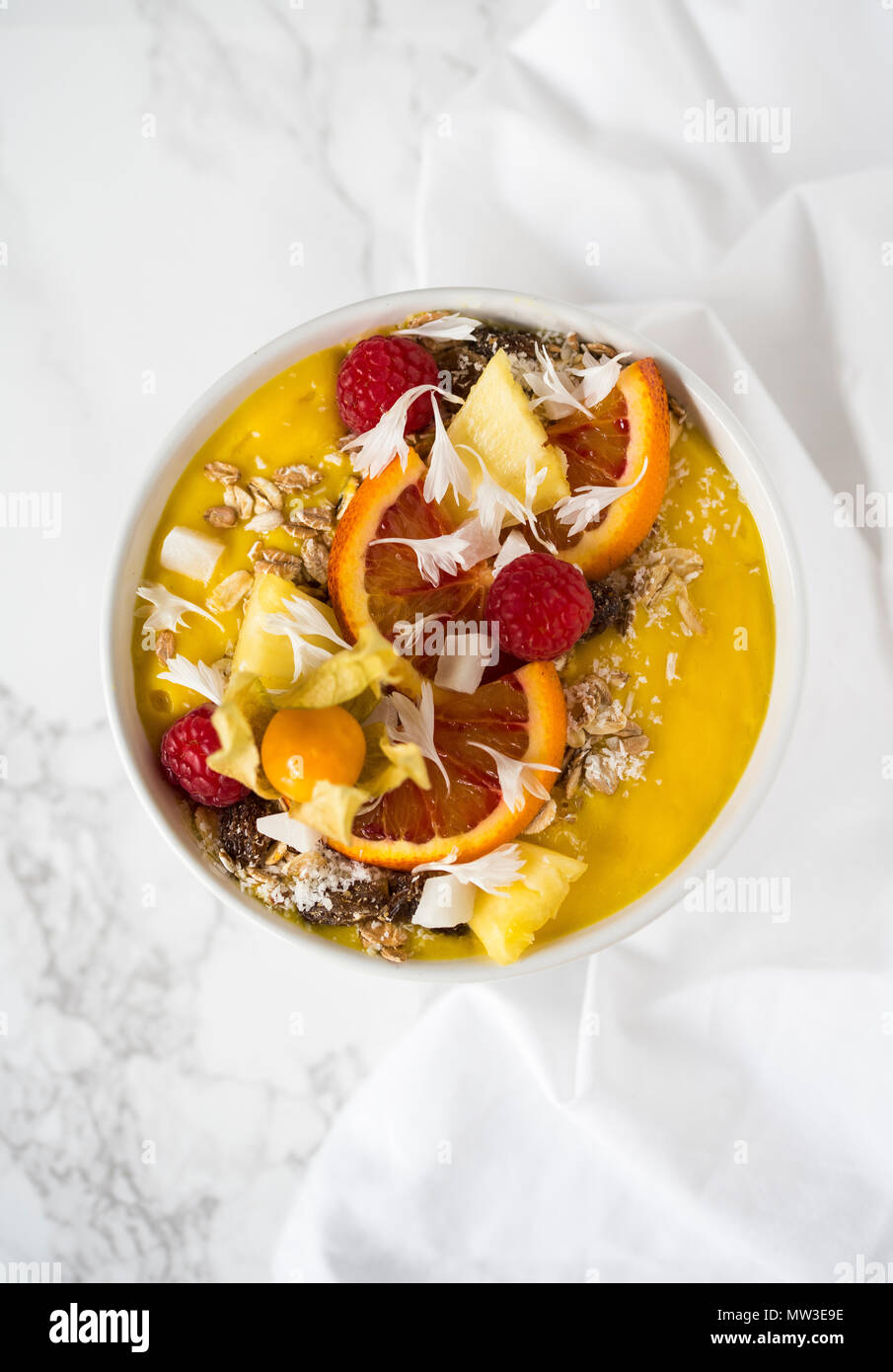 Smoothie mangue jaune à décor d'granola, baies, fruits, flocons de noix de coco sur une base en marbre blanc Banque D'Images