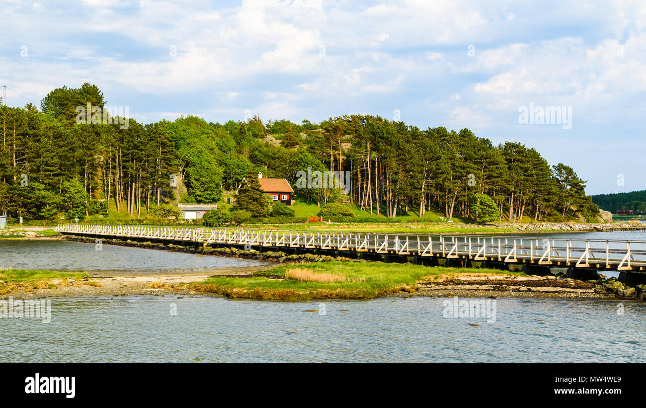 Joli paysage côtier avec une longue passerelle au-dessus de l'eau peu profonde et une maison dans les arbres en arrière-plan. Arod près de Kungalv, Suède. Banque D'Images