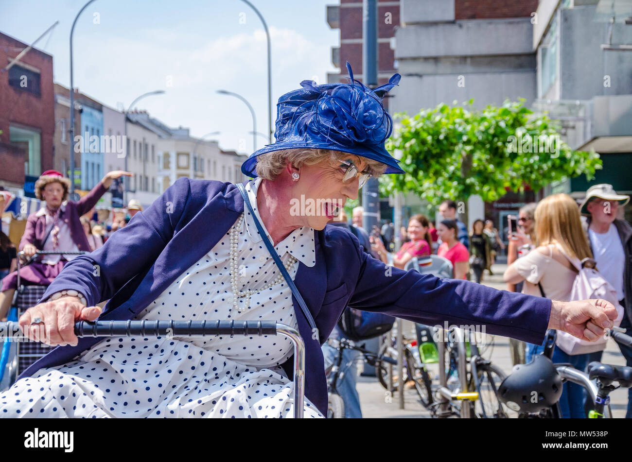 Un homme habillé comme une vieille femme équitation un panier est en fait un artiste de rue émerveillant à la Hammersmith & Fulham Marché de Printemps Banque D'Images