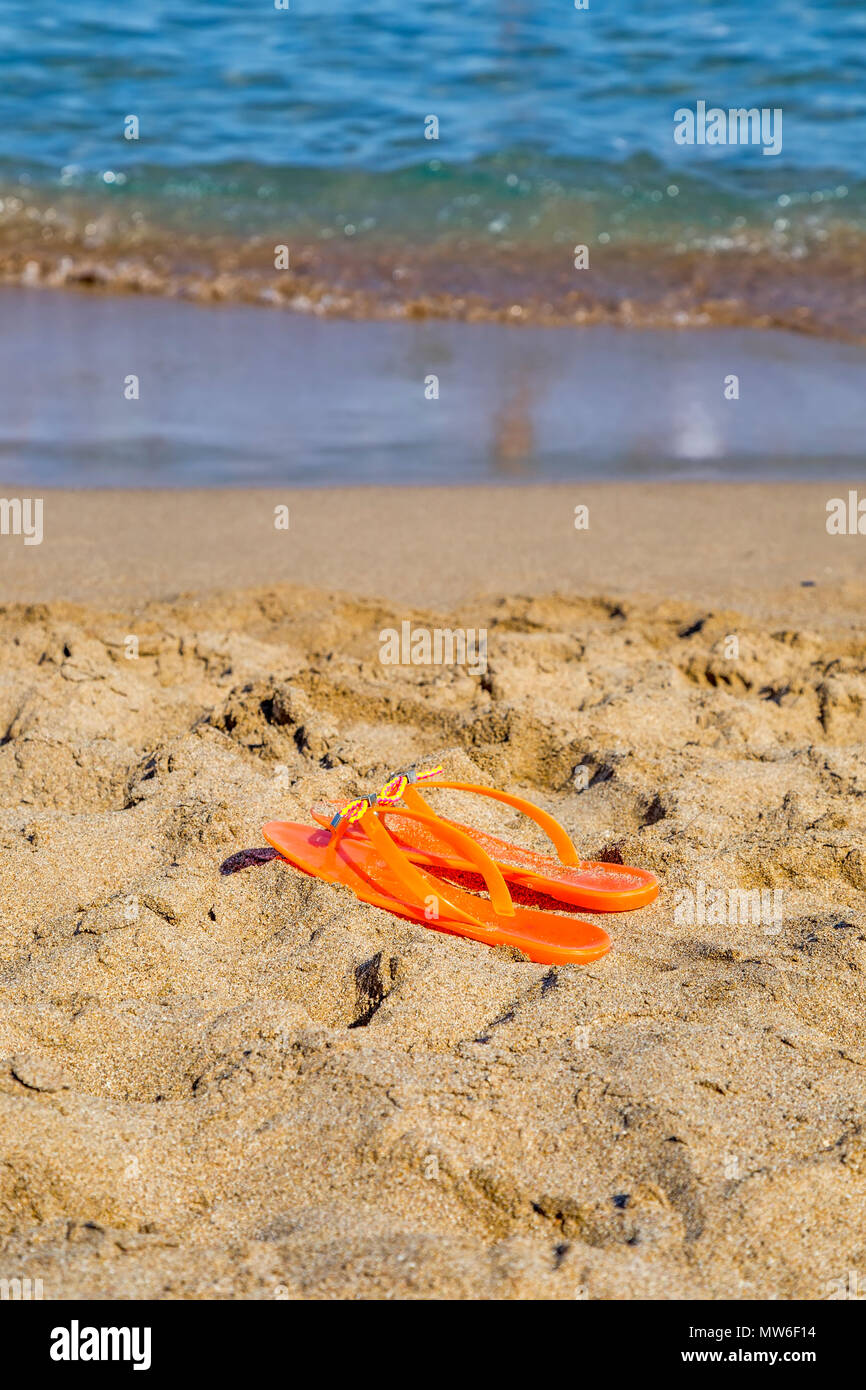 Paire de tongs orange sur la plage de sable fin. Banque D'Images