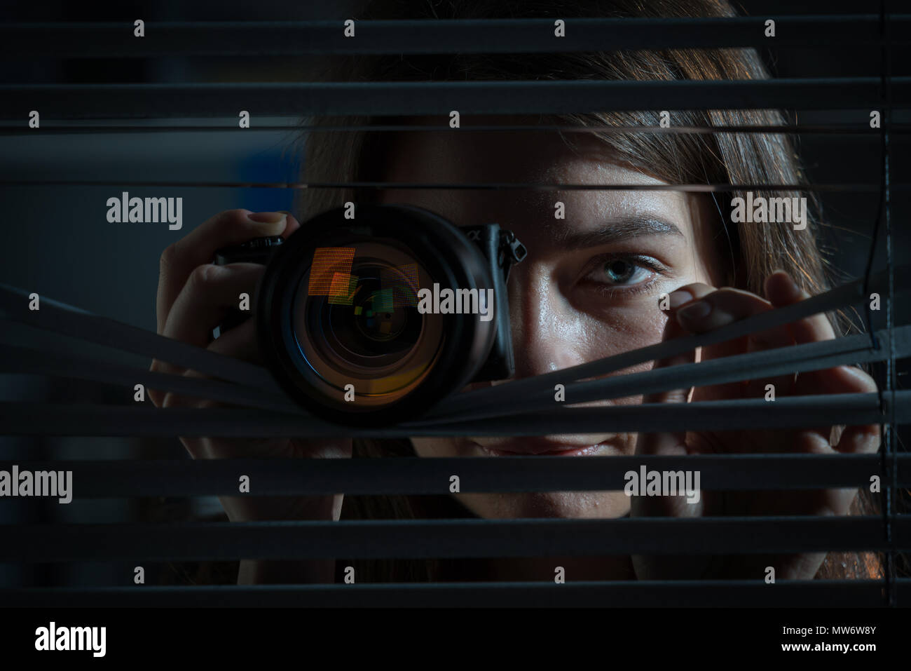 Jeune femme photographe Paparazzi capture d'une photo d'un air suspicieux autour d'une jalousie tout en utilisant un appareil photo Banque D'Images