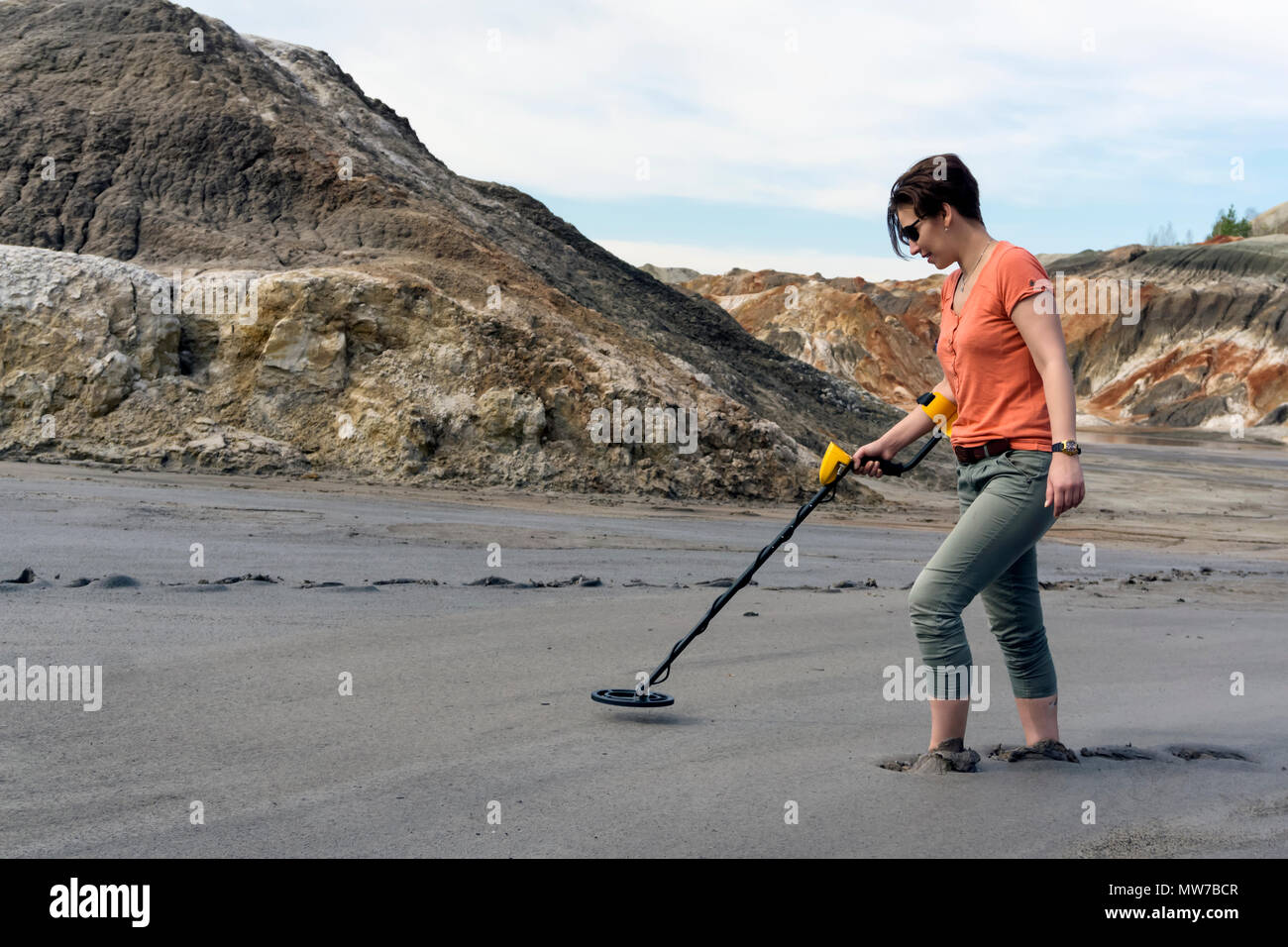 Femme dans un canyon désert jusqu'aux chevilles dans la boue des recherches avec un détecteur de métal Banque D'Images