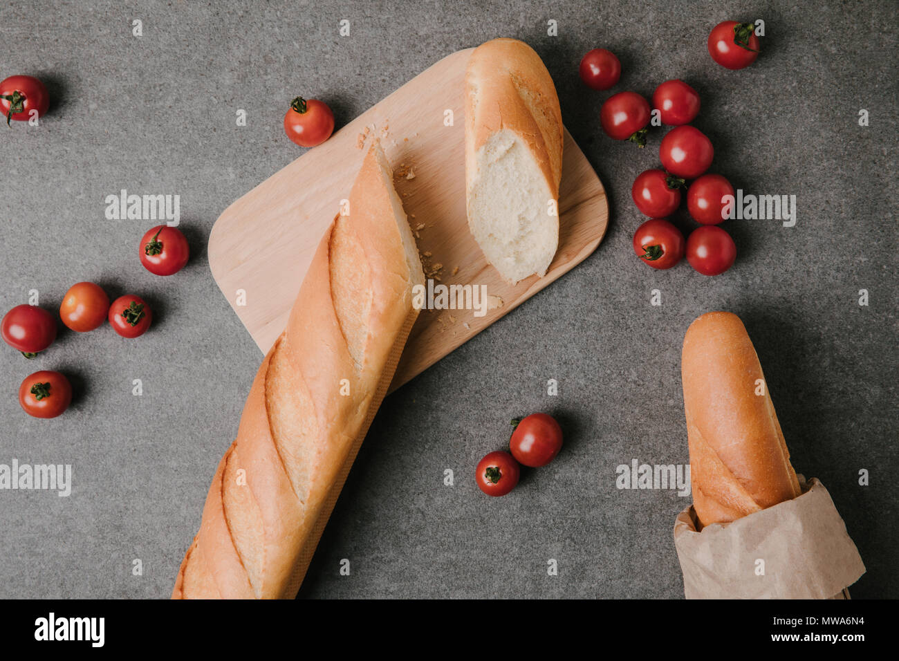 Vue de dessus de baguettes, planche de bois et tomates fraîches sur gris Banque D'Images