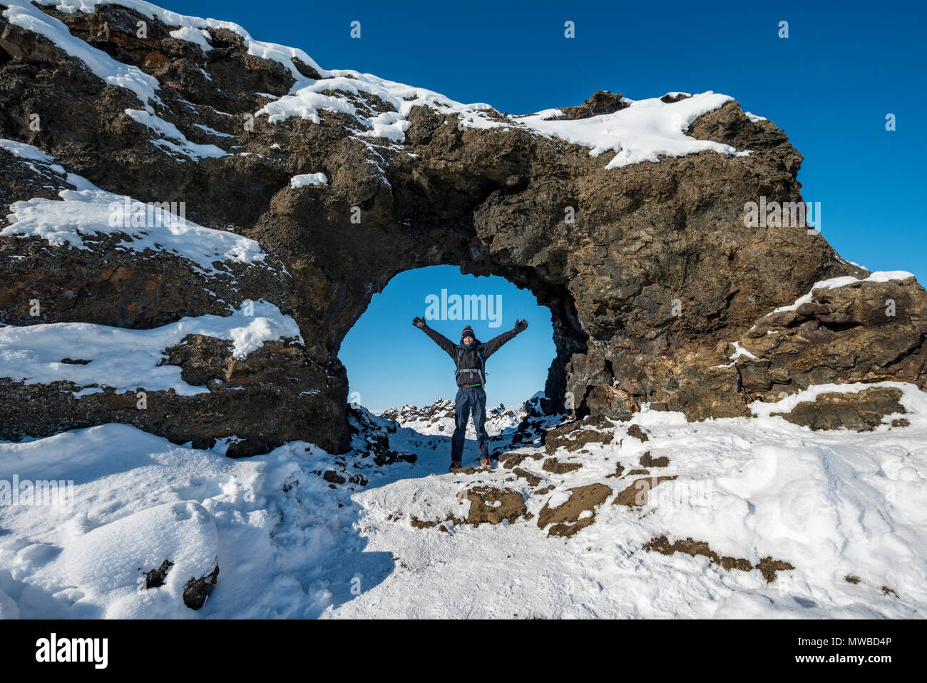 Homme debout en face d'un champ de lave, arche rocheuse couverte de neige, paysage volcanique Krafla, Dimmuborgir National Park Banque D'Images