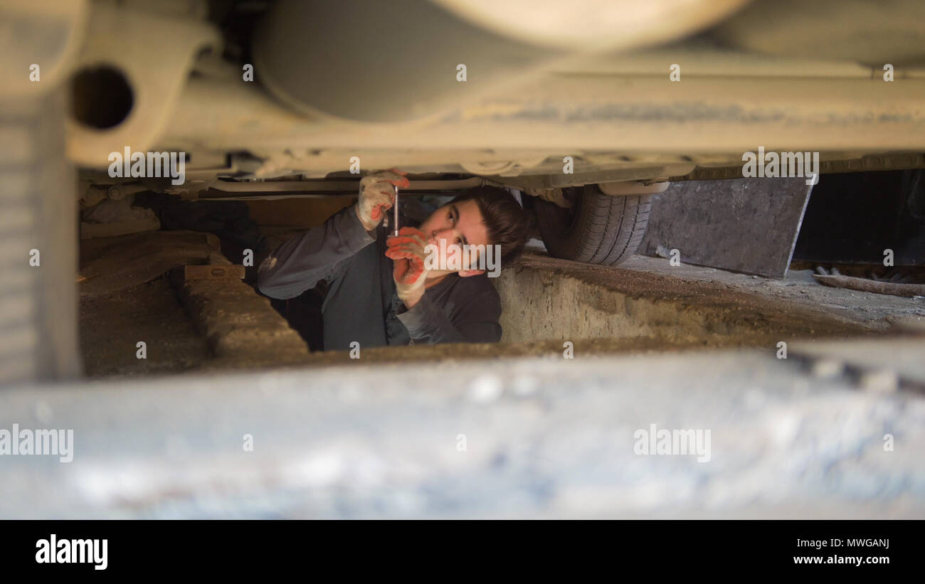 Mécanicien mâle sous une voiture pour atteindre un tournevis dans le garage Banque D'Images