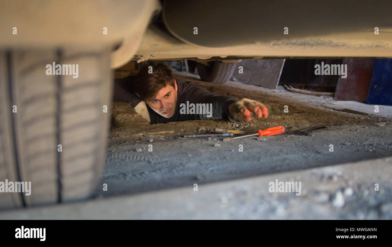 L'homme sous une voiture pour atteindre un tournevis pour la réparation de voiture Banque D'Images