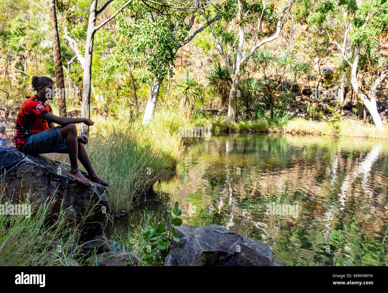 Un mâle adolescent autochtone assis sur un rocher à côté d'une natation dans le trou de l'Australie. WA Kimberley Banque D'Images
