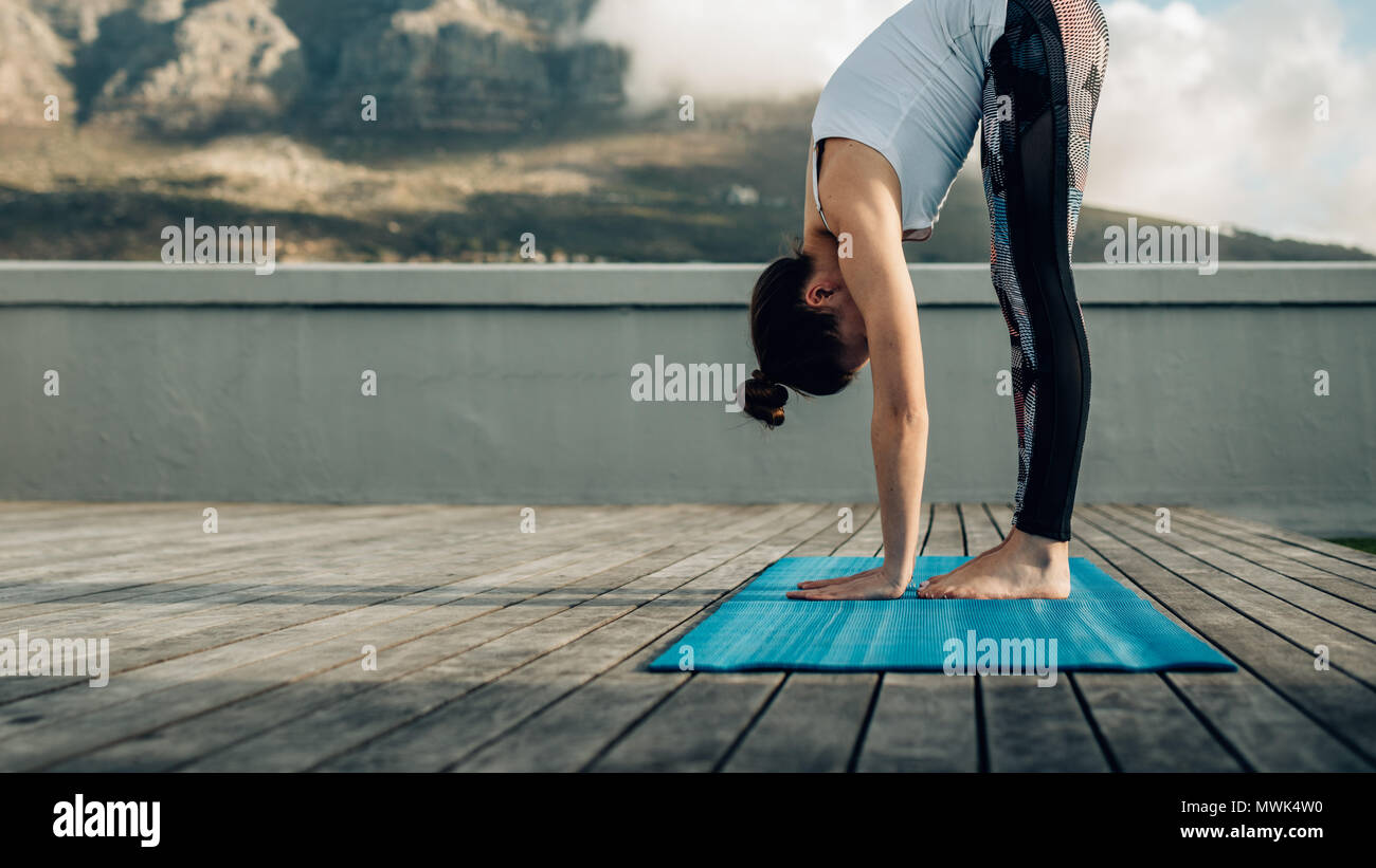 Femme pratiquant des positions de yoga sur la terrasse de sa maison. femme de fitness dans une posture de yoga se penchant vers le bas avec les paumes touchant le sol. Banque D'Images