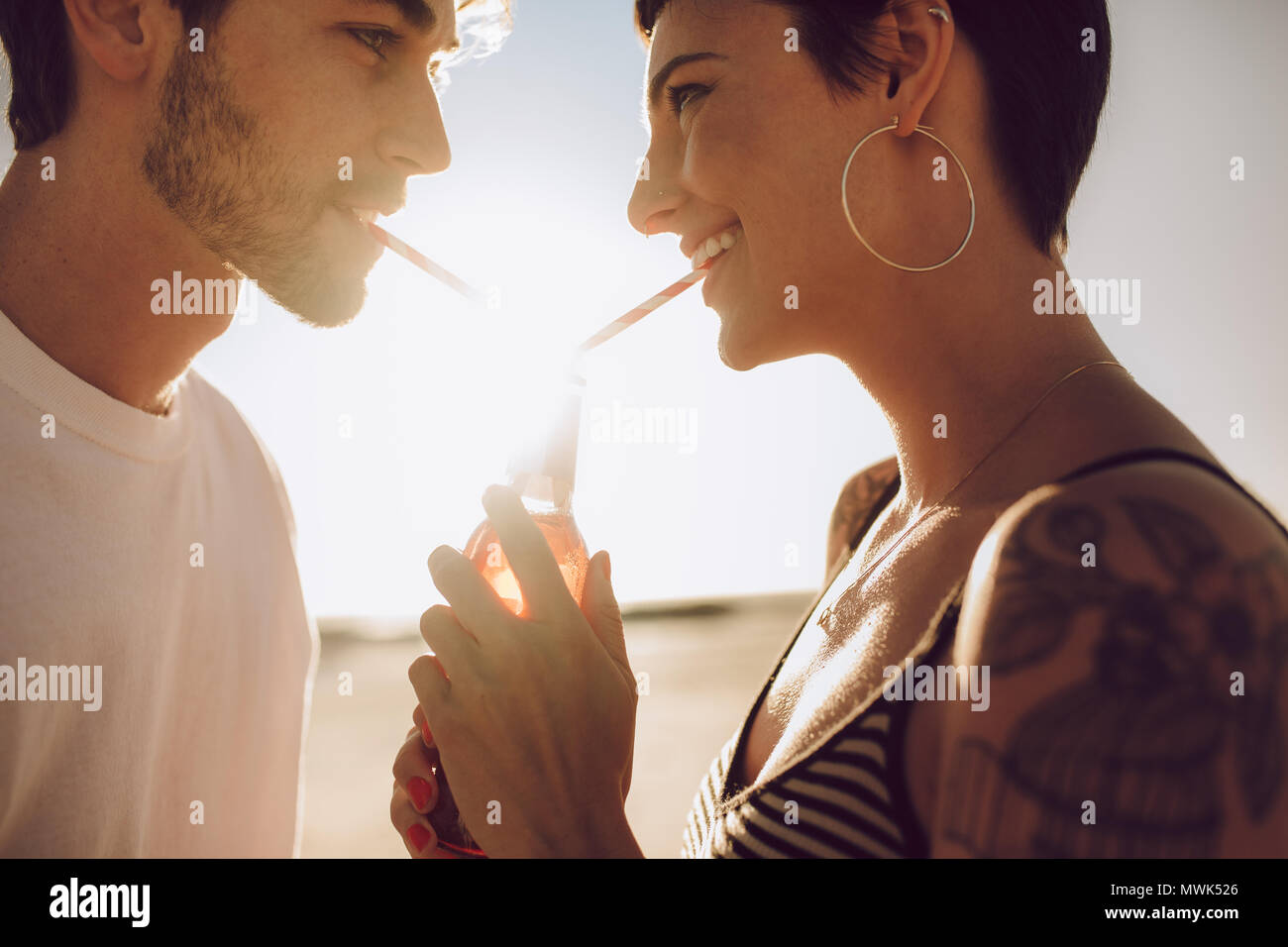 Close up of smiling couple dans l'amour de boisson potable une bouteille en verre avec de la paille. L'homme et la femme jouissant de boire boisson froide à l'extérieur sur une d'été Banque D'Images