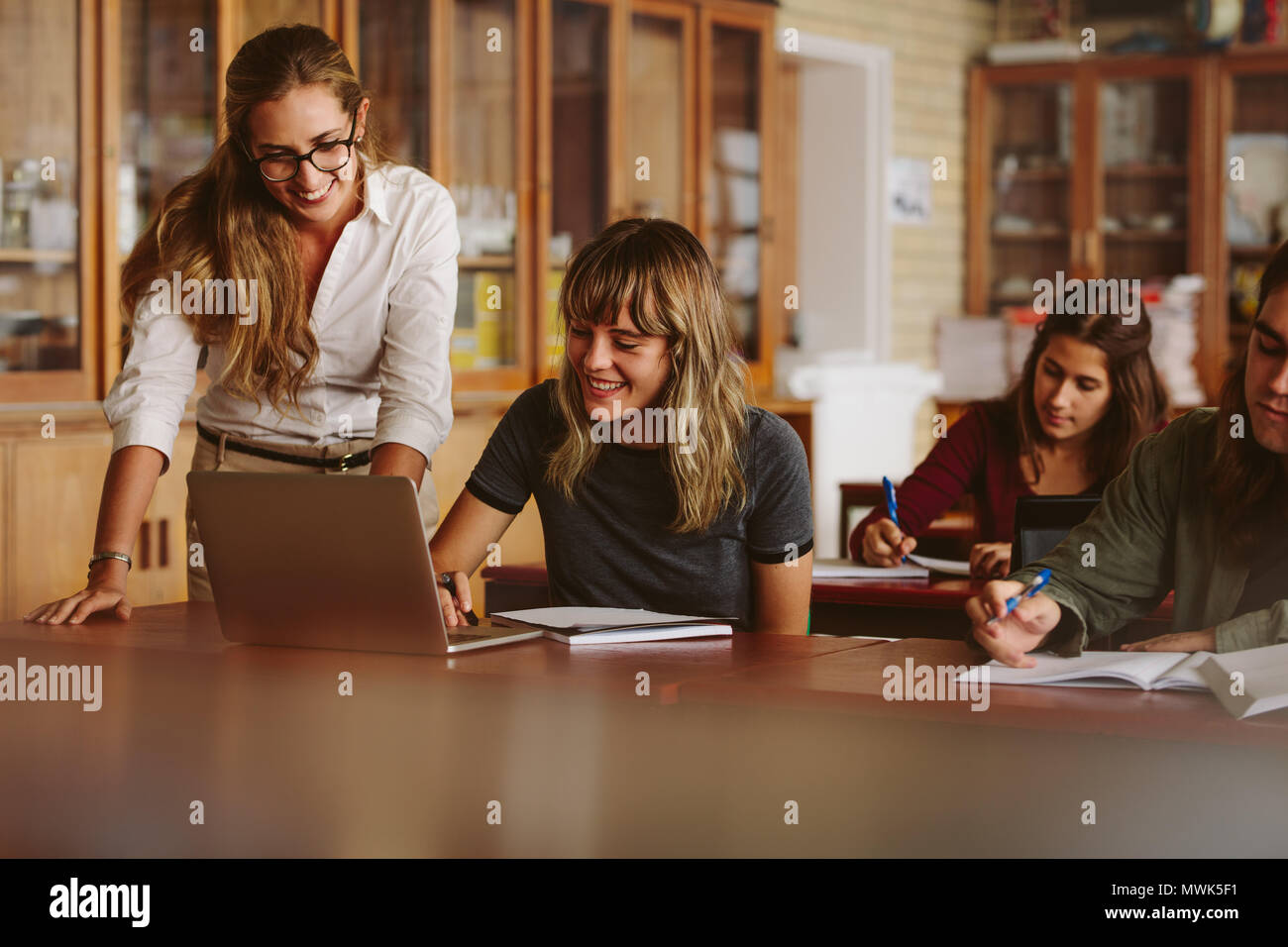 Professionnels enseignant aider son élève à l'école secondaire. Femme à l'aide d'un ordinateur portable avec son professeur par permanent et smiling in classroom. Banque D'Images
