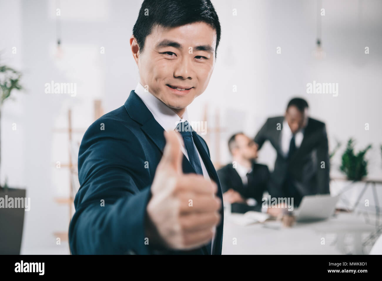 Asian businessman showing thumb up with blurred collègues de contexte Banque D'Images