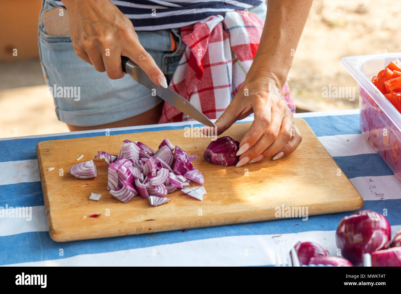 Femme mains slicing oignons rouges sur la planche à découper en bois. Chef chopping un oignon rouge avec un couteau pour une salade de légumes. Street Food Festival. Banque D'Images