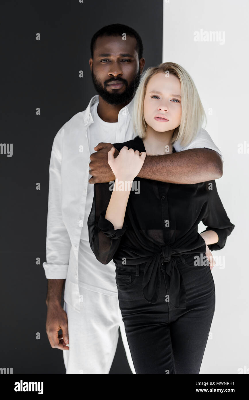African American Boyfriend hugging copine blonde près de mur noir et blanc Banque D'Images