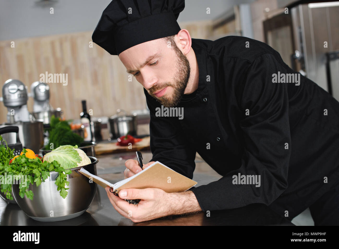 Vue latérale du beau cuisinier, l'écriture de nouvelle recette de cuisine au restaurant de l'ordinateur portable Banque D'Images