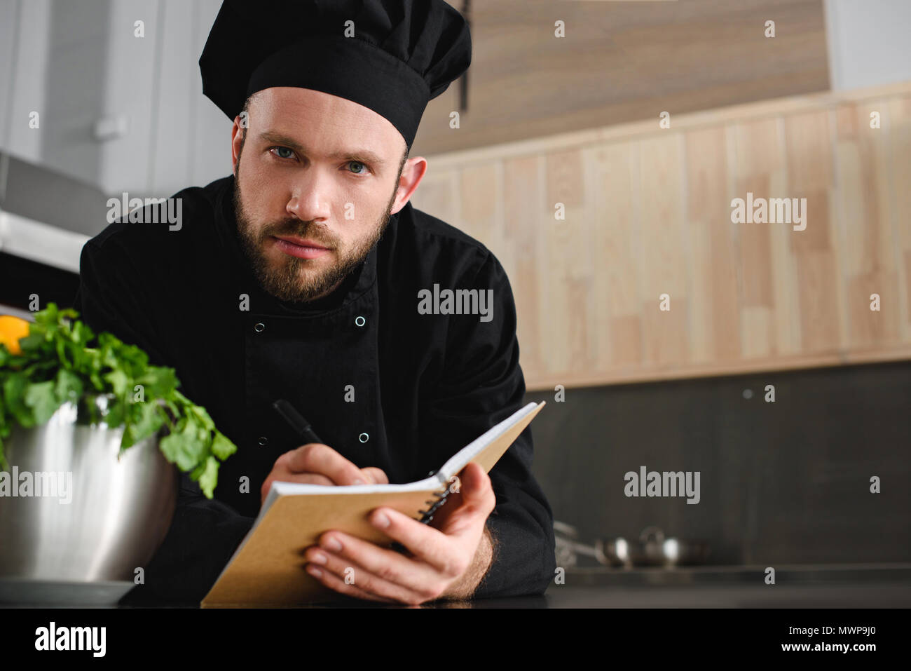 Beau chef de l'écriture de nouvelle recette à l'ordinateur portable au restaurant cuisine et looking at camera Banque D'Images