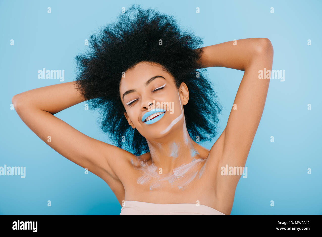 Souriante jeune femme avec maquillage créatif et lèvres bleu sur bleu isolé Banque D'Images