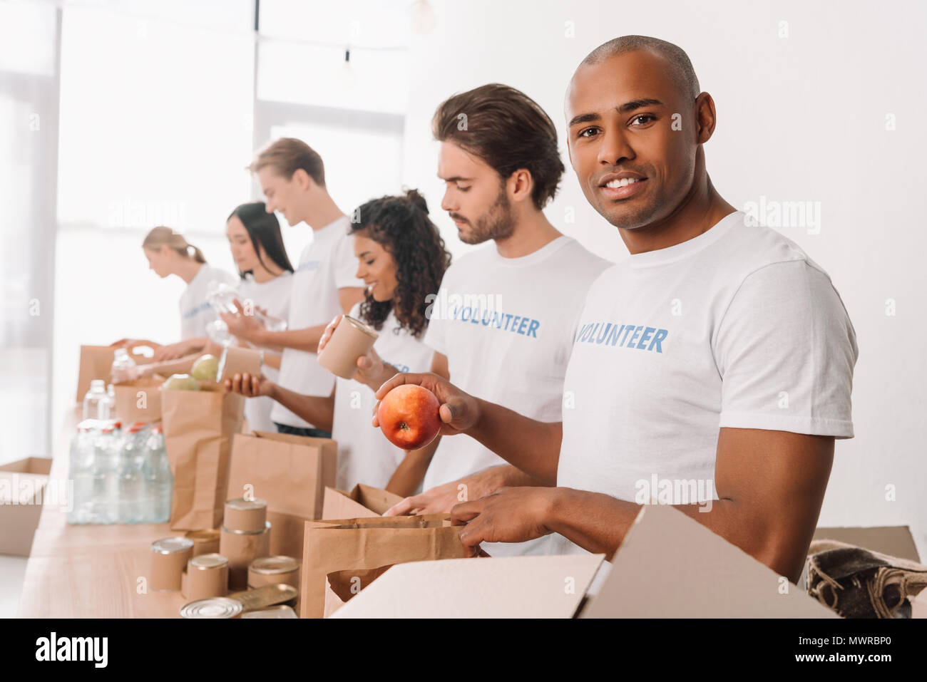 African American volunteer conserve des aliments dans des sacs avec muriethnic groupe de collègues Banque D'Images