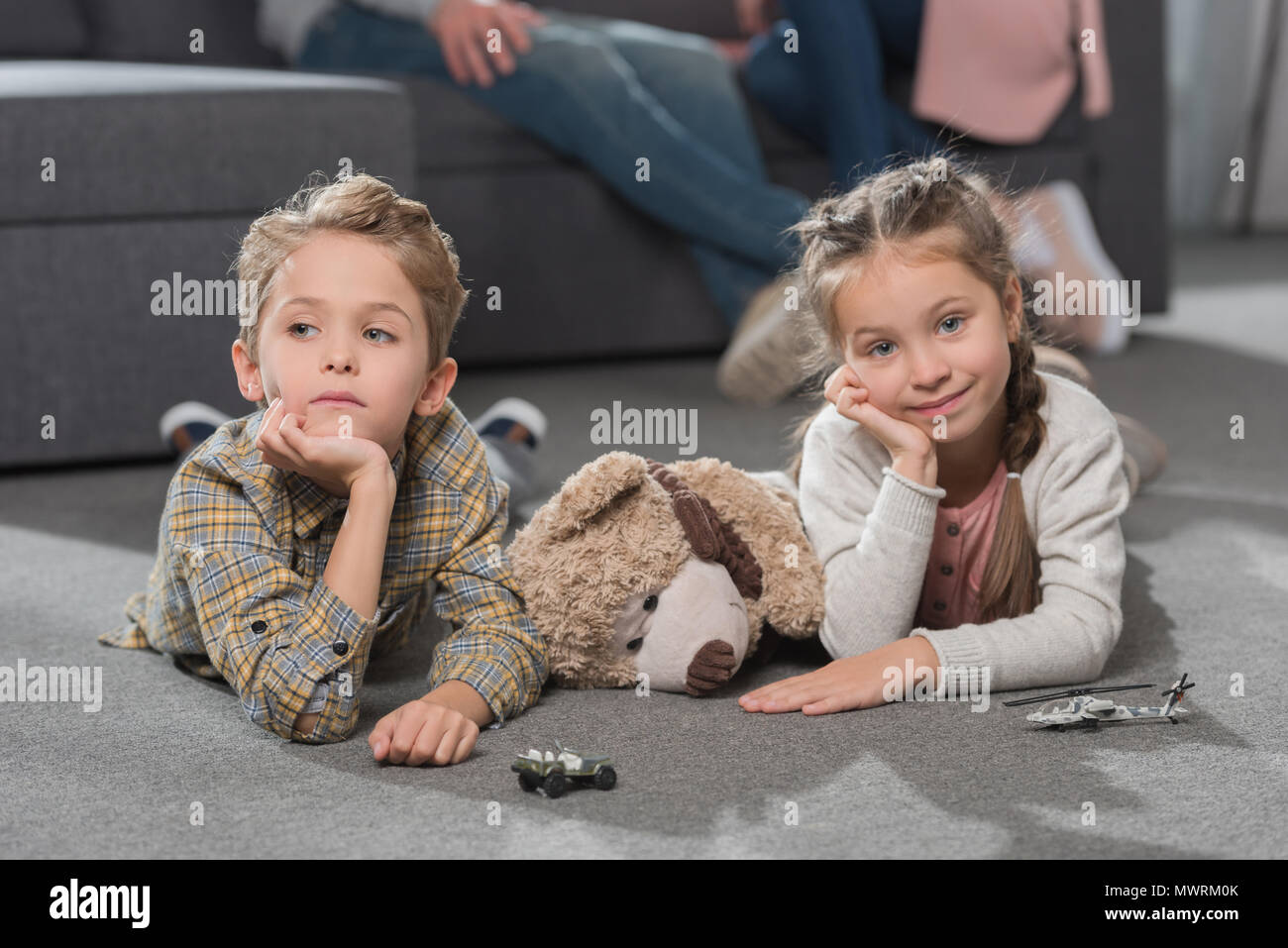 Deux petits enfants couchés sur marbre dans la salle de séjour avec des jouets et posant les mains sur le menton Banque D'Images