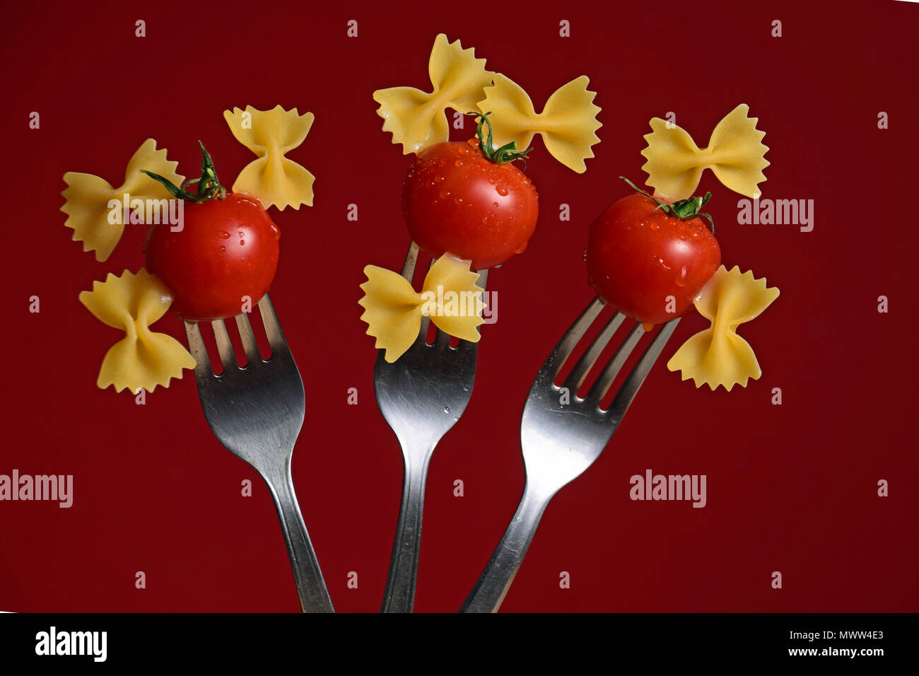 Tomates cerise et Bow tie passé sur fourches sur un fond rouge Banque D'Images