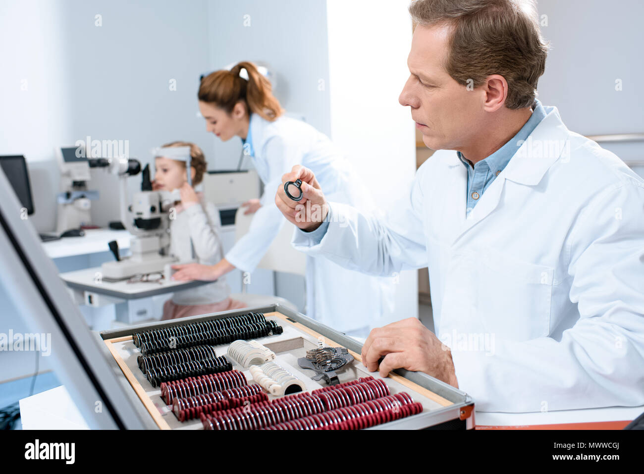 Opticien lentilles holding pour le procès le châssis tout en collègue examinant kid avec test de champ visuel Banque D'Images