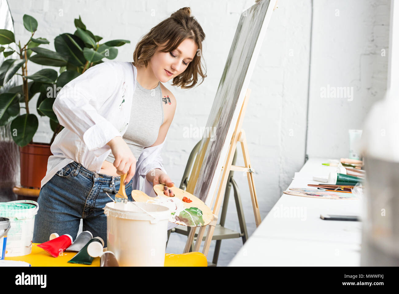 Jeune fille inspirée dunks un pinceau dans la peinture dans le Light Studio Banque D'Images