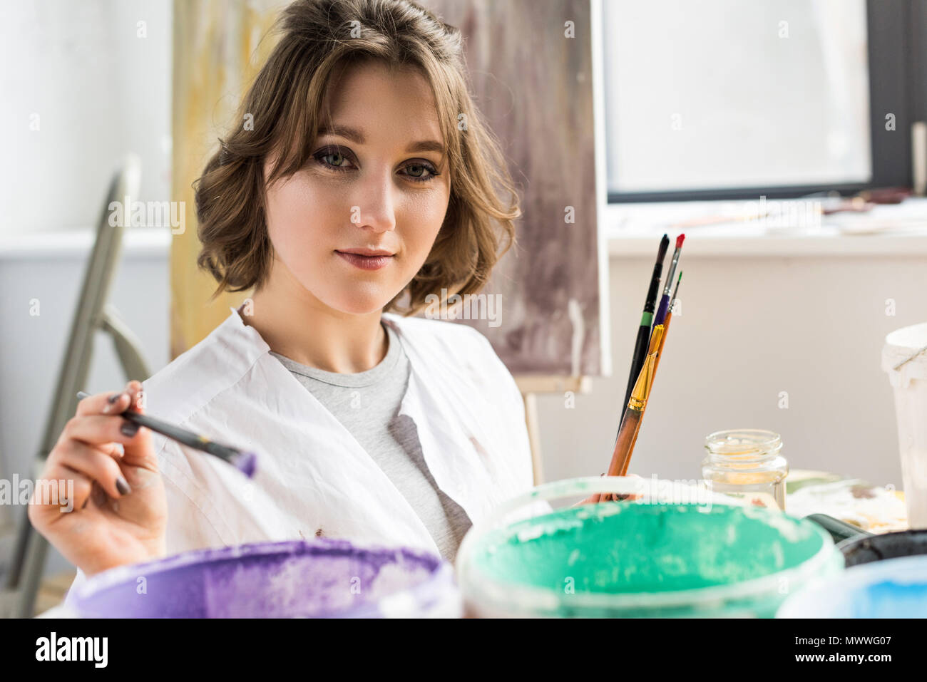 Jeune fille artistique dunks un pinceau dans la peinture dans le Light Studio Banque D'Images