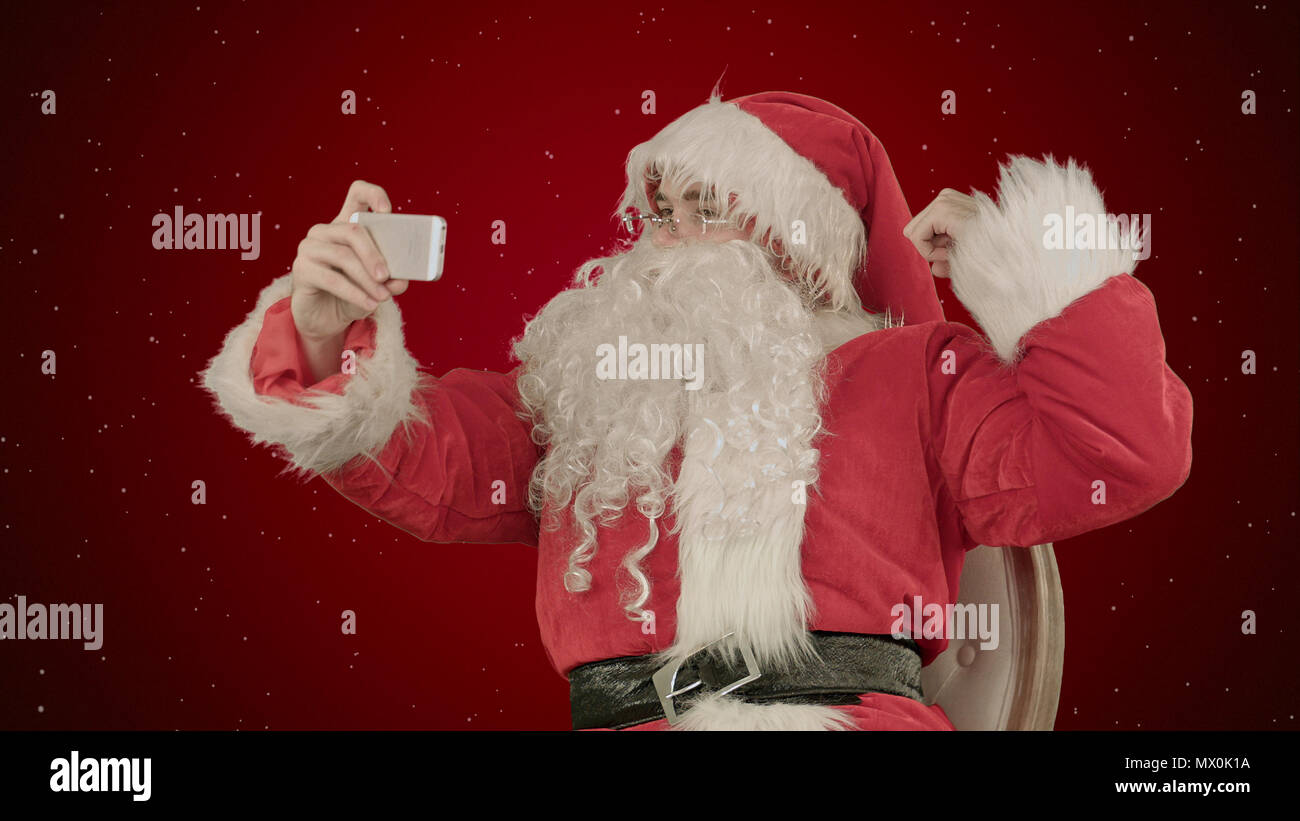 Santa Claus prendre un sur fond rouge selfies avec la neige. Tourné au sein du comité professionnel cru avec une plage dynamique élevée. Vous pouvez l'utiliser par exemple dans votre vi commercial Banque D'Images