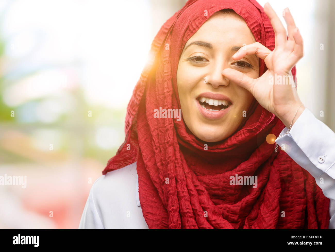 Jeune femme arabe portant le hijab looking at camera entre ses doigts dans  un geste ok. L'imitation des jumelles, de beaux yeux et sourire Photo Stock  - Alamy