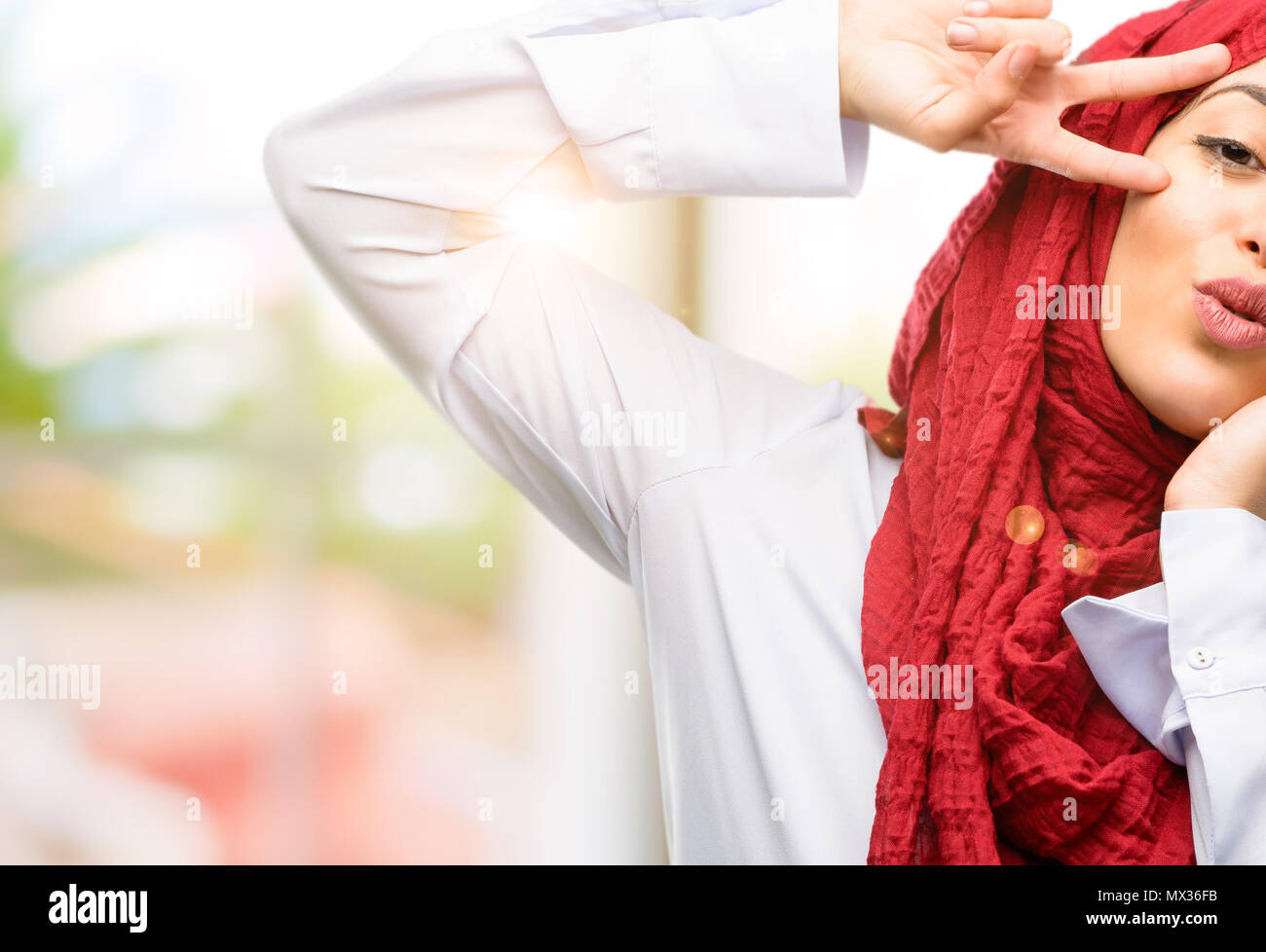 Jeune femme arabe portant le hijab à la caméra à l'intermédiaire de ses  doigts en un clin d'œil le geste de la victoire et en soufflant un baiser  Photo Stock - Alamy