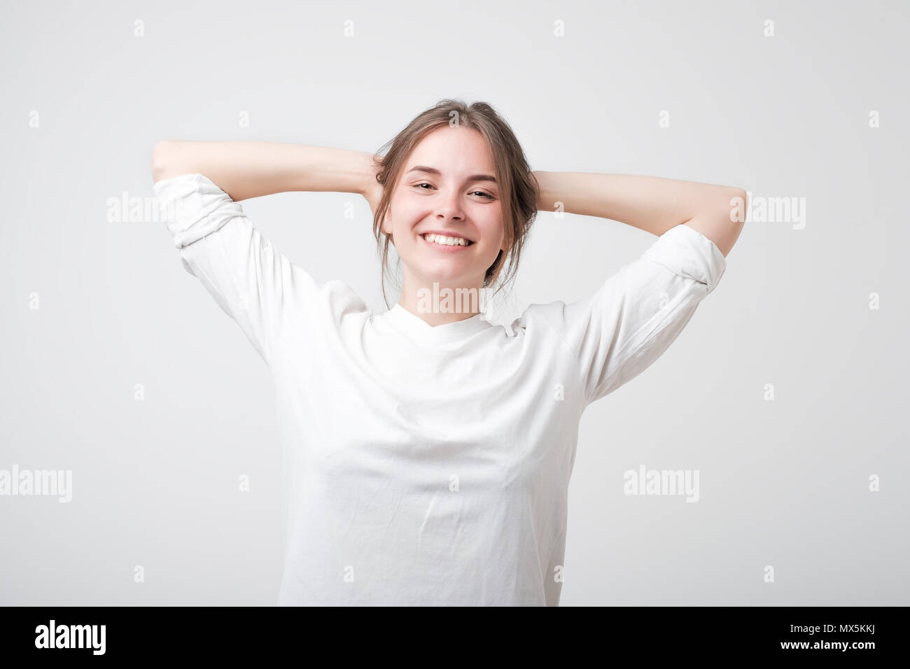 L'insouciance heureuse young caucasian woman in white t-shirt avec un sourire mignon posant avec ses mains sur sa tête. Banque D'Images